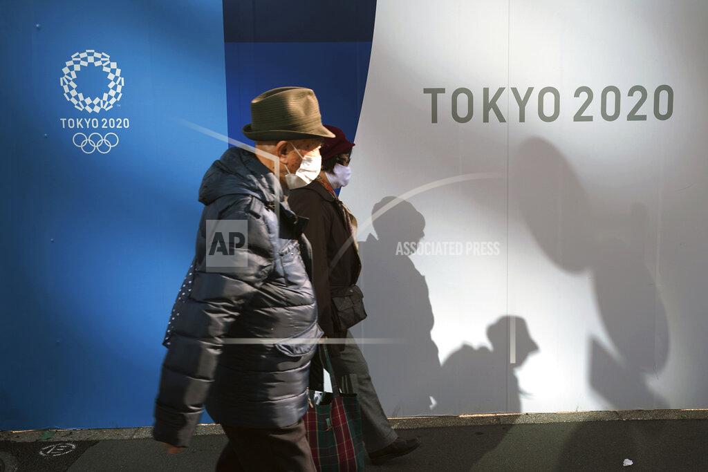 A man and a woman wearing protective masks to help curb the spread of the coronavirus walk in front of logos of Tokyo 2020 Olympics Monday, Nov. 30, 2020, in Tokyo. (AP Photo/Eugene Hoshiko)