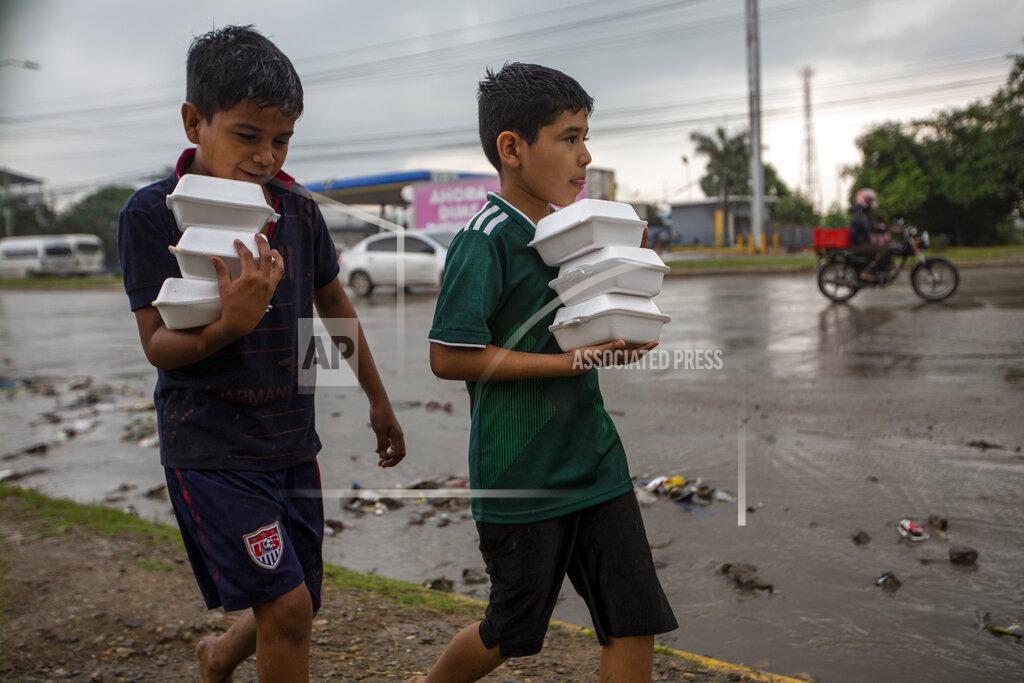 Moises Castillo Youths carry donated hot meals back to their tents alongside a highway where they live with others after last year's hurricanes Eta and Iota left their family's homeless in San Pedro Sula, Honduras, Tuesday, Jan. 12, 2021. The World Food Program says the number of Hondurans facing food insecurity is 3 million, six times higher than before. (AP Photo/Moises Castillo)