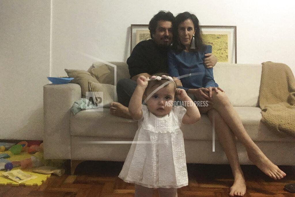 In this May 29, 2020, photo, Associated Press writer Mauricio Savarese sits with his partner Luisa Belchior as their daughter Carolina, 1, looks on in their home in Sao Paulo. Savarese and Belchior paid for the visit of a notary officer to get their civil union certificate, like many Brazilians that want to avoid bigger risk of contracting COVID-19. (AP Photo/Mauricio Savarese)
