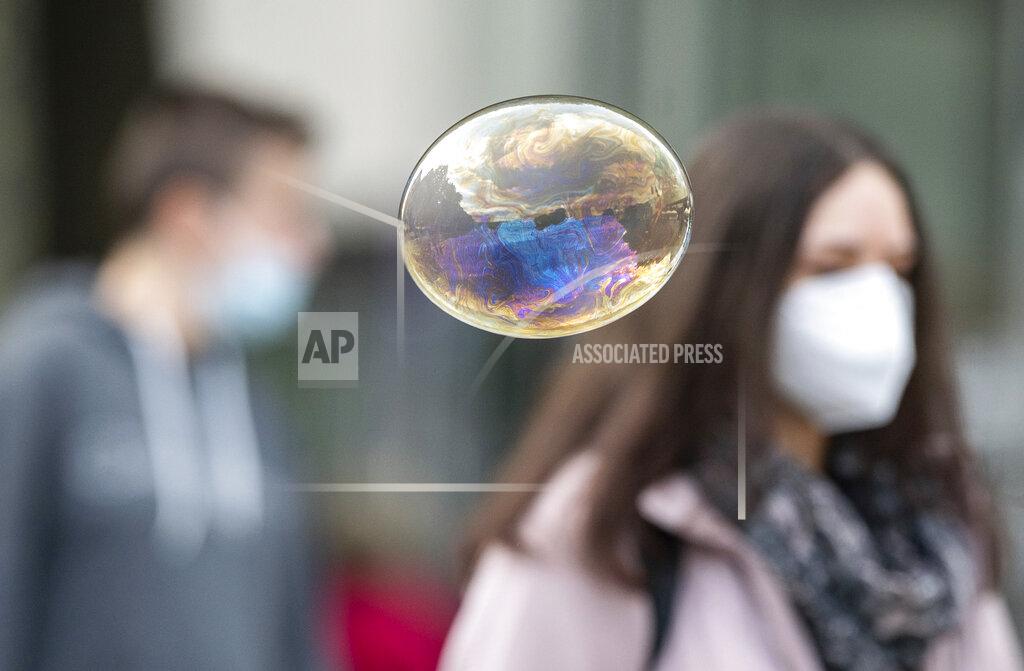 Sebastian Gollnow A soap bubble flies in front of people with mouth and nose protection in Stuttgart, Germany, Friday, Oct. 9, 2020. Chancellor Merkel is discussing the situation with the mayors of the eleven largest German cities in view of the sharp rise in corona figures. (Sebastian Gollnow/dpa via AP)