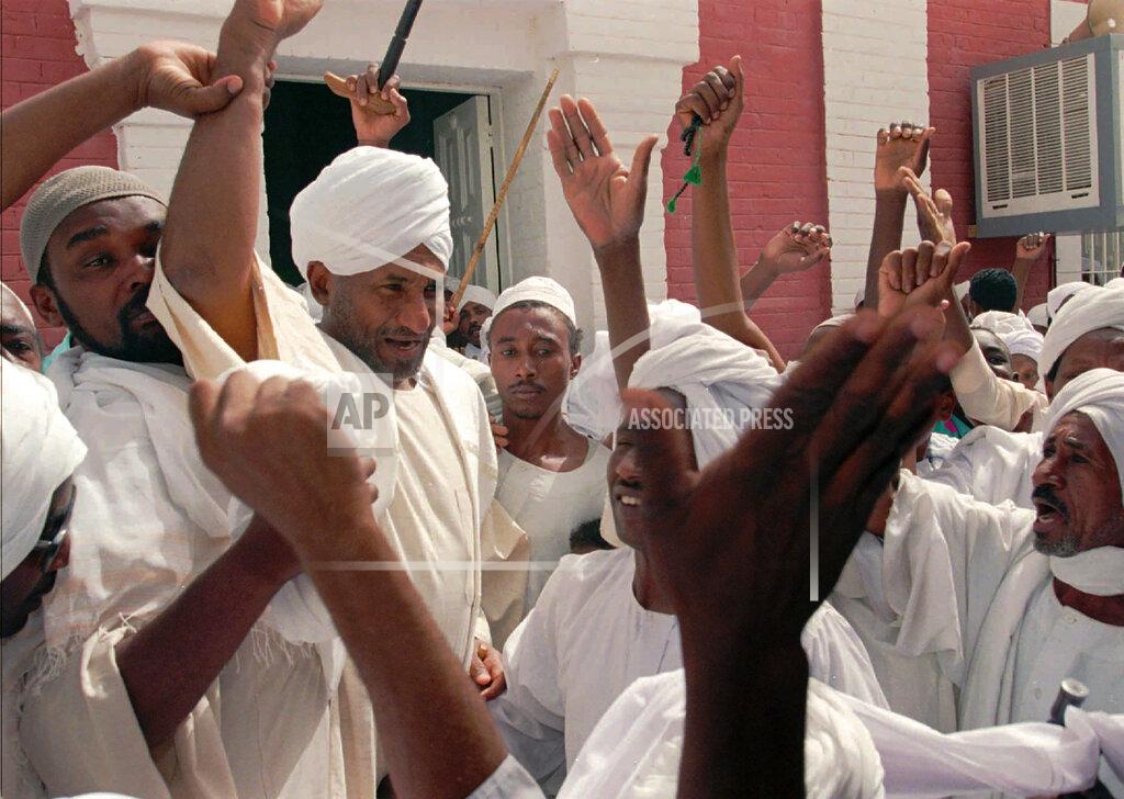 Jean-Marc Bouju FILE - In this March 22, 1996 file photo, then opposition leader Sadiq Al-Mahdi, center left, is cheered by supporters as he walks out of the Wad Nubawi Mosque in Khartoum, Sudan. Former Sudanese prime minister and head of the country’s largest political party, Sadiq al-Mahdi, 84, died of COVID-19 late on Wednesday, Nov. 25, 2020, at a hospital in the United Arab Emirates, his party said. (AP Photo/Jean-Marc Bouju, File)
