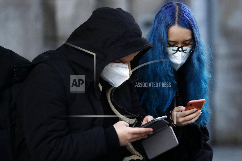 Frank Augstein A young couple wearing face masks to prevent the spread of coronavirus look at their smartphones in Liverpool, England, Wednesday, Oct. 14, 2020. (AP Photo/Frank Augstein)