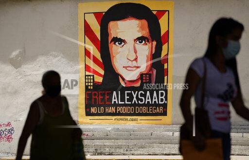 FILE - In this Thursday, Sept 9, 2021, file photo, pedestrians walk near a poster asking for the freedom of Colombian businessman and Venezuelan special envoy Alex Saab, in Caracas, Venezuela. Saab, a top fugitive close to Venezuela's socialist government has been put on a plane to the U.S. to face money laundering charges, a senior U.S. official confirmed Saturday, Oct. 16, 2021. (AP Photo/Ariana Cubillos, File)