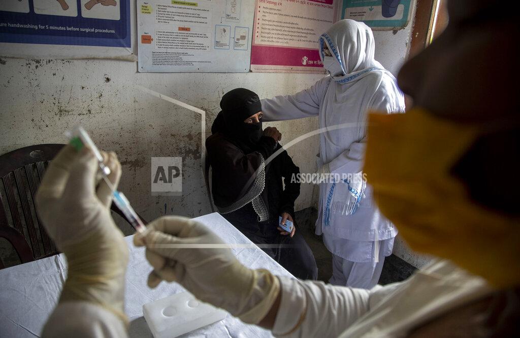 Anupam Nath A health worker readies a COVID-19 vaccine as another comforts an elderly woman at a health center in Bahakajari village in an interior part of Indian northeastern state of Assam, India, Tuesday, March 23, 2021. In India, workers recently trekked to the tiny village to start vaccinating its nearly 9,000 residents. (AP Photo/Anupam Nath)