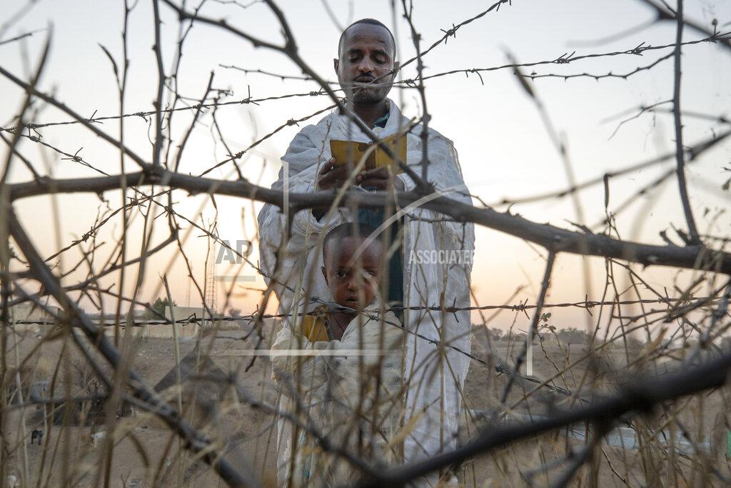 An Orthodox Christian refugee who fled the conflict in the Ethiopia's Tigray region reads prayers with his son in front of a church at the Hamdeyat Transition Center near the Sudan-Ethiopia border, eastern Sudan, Tuesday March 16, 2021. Political tensions between Ethiopian Prime Minister Abiy Ahmed's government and the Tigray leaders who once dominated the country's government exploded in November into war. (AP Photo/Nariman El-Mofty)