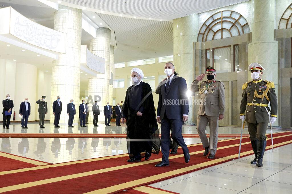 In this photo released by the official website of the office of the Iranian Presidency, Iraqi Prime Minister Mustafa al-Kadhimi, center, is welcomed by President Hassan Rouhani, center left, as they wear protective face masks to help prevent spread of the coronavirus, during an official arrival ceremony, in Tehran, Iran, Tuesday, July 21, 2020. (Iranian Presidency Office via AP)