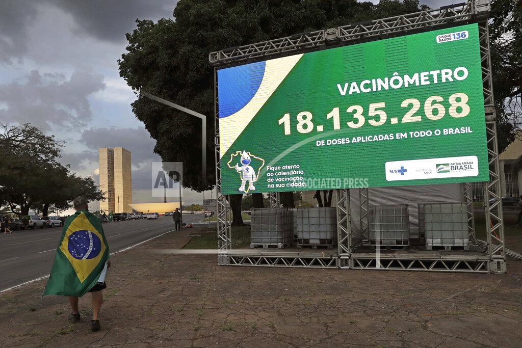Eraldo Peres A demonstrator wearing a Brazilian national flag as a cape for a rally in support of Brazil's President Jair Bolsonaro, walks past a billboard presenting the number of COVID-19 vaccines administered to encourage others to get the vaccine, outside the Health Ministry in Brasilia, Brazil, Tuesday, March 30, 2021. (AP Photo/Eraldo Peres)