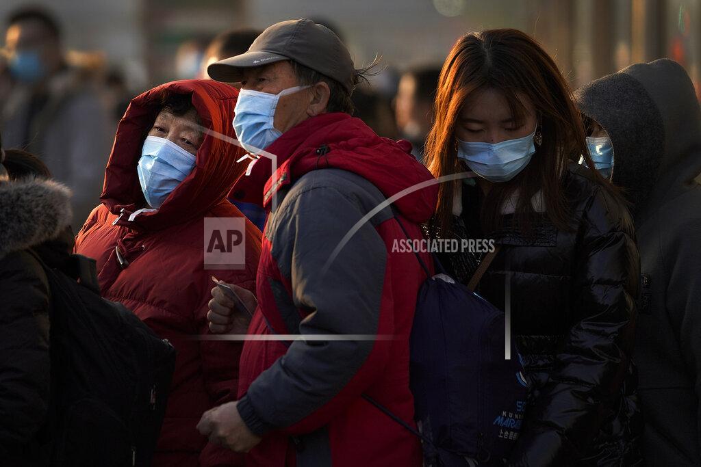 Andy Wong A woman wearing a face mask to help curb the spread of the coronavirus walks by a masked elderly couple wait for their bus at a bus stand in Beijing, Sunday, Dec. 6, 2020. Provincial governments across China are placing orders for experimental, domestically made coronavirus vaccines, though health officials have yet to say how well they work or how they may reach the country's 1.4 billion people. (AP Photo/Andy Wong)