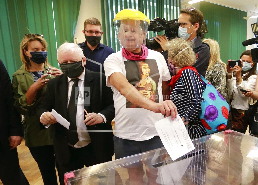 Uncredited Leader of Poland's right-wing ruling party Jaroslaw Kaczynski, left, wearing a face mask for protection against the coronavirus, casts his ballot in tight presidential election runoff in Warsaw, Poland, on Sunday, July 12, 2020, next to a man wearing a face mask of Kaczynski's likeness. The ruling Law and Justice party is backing the reelection bid of incumbent conservative President Andrzej Duda, against the liberal Warsaw Mayor Rafal Trzaskowski. Latest opinion polls suggested that the runoff will be decided by a very narrow margin. (AP Photo)