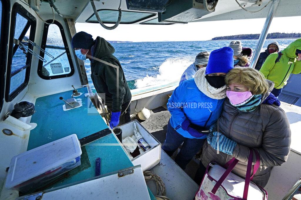 Robert F. Bukaty Nurses Kathy Cheney, wearing hat, and Maureen Giffen huddle on a wet and windy ride aboard a lobster boat on the way to set up a COVID-19 vaccination clinic, Friday, March 19, 2021, on Great Cranberry Island, Maine. Getting the vaccine to the world's farthest corners means delivering it by boat to Maine's islands, traveling by snowmobile to villages in Alaska and navigating complex waterways in Brazil's Amazon. (AP Photo/Robert F. Bukaty)