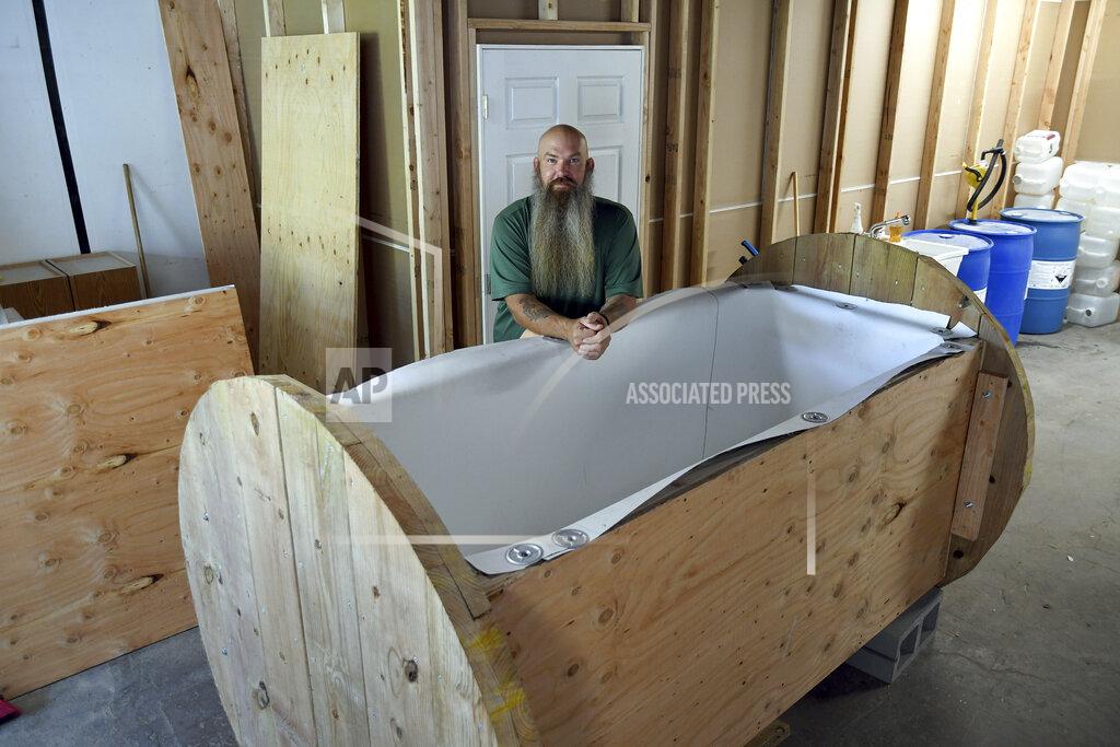 Thomas Peipert In this Wednesday, Aug. 11, 2021, photo, Seth Viddal, who co-owns The Natural Funeral, stands behind a nearly completed human body composting vessel in Arvada, Colo. On Sept. 7, Colorado became the second state after Washington to allow human body composting, and Oregon will allow the practice beginning next July. The vessel will be packed with wood chips and straw and will be able to compost a body in six months. About the size of a standard grave, the rectangular insulated wooden box is lined with waterproof roofing material and packed with wood chips and straw. Two large spool wheels on either end allow it to be rolled across the floor, providing the oxygenation, agitation and absorption required for a body to compost. (AP Photo/Thomas Peipert)
