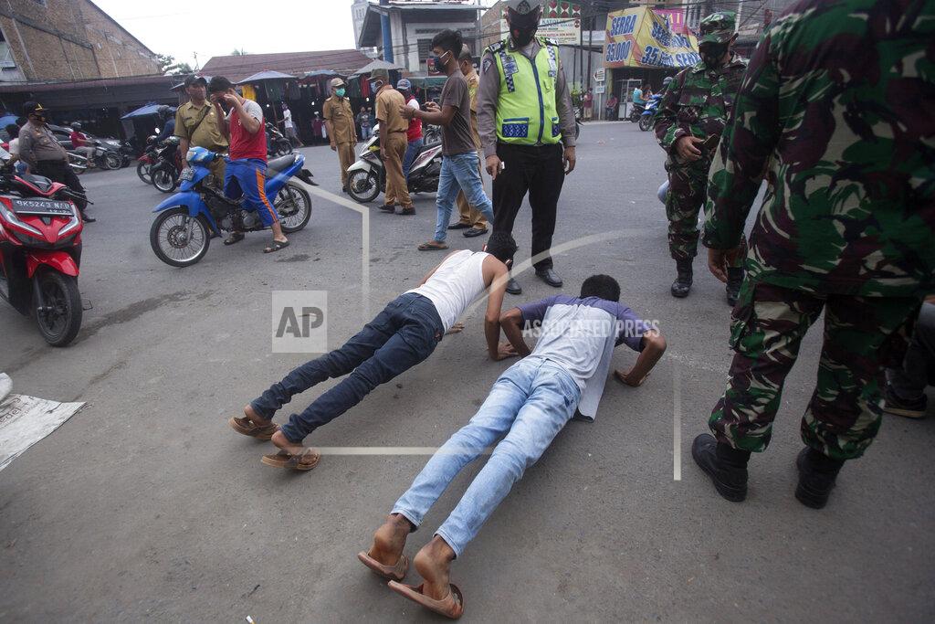 Binsar Bakkara An Indonesian policeman and soldiers watch men do push-ups as a punishment for violating city regulation requiring people to wear face masks in public places as a precaution against coronavirus outbreak, in Medan, North Sumatra, Indonesia, Wednesday, Sept. 23, 2020. (AP Photo/Binsar Bakkara)