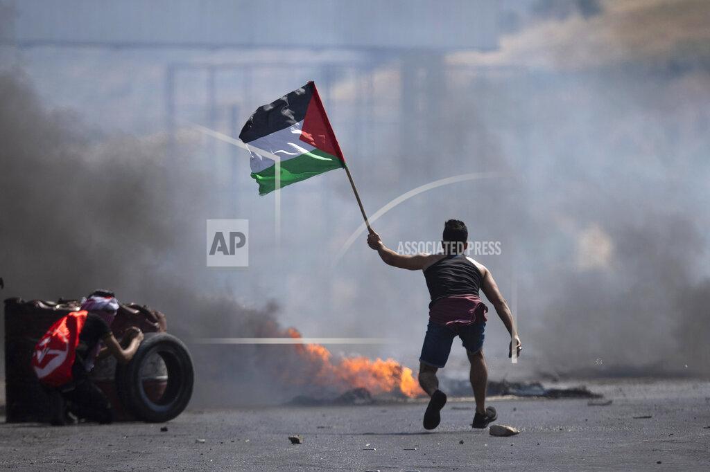 Majdi Mohammed A protester waves the Palestinian flag during clashes with the Israeli forces at the Hawara checkpoint, south of the West Bank city of Nablus, Friday, May 14, 2021. Health officials say several Palestinians were killed by Israeli army fire, at protests that took place in several locations across the West Bank of Friday. (AP Photo/Majdi Mohammed)