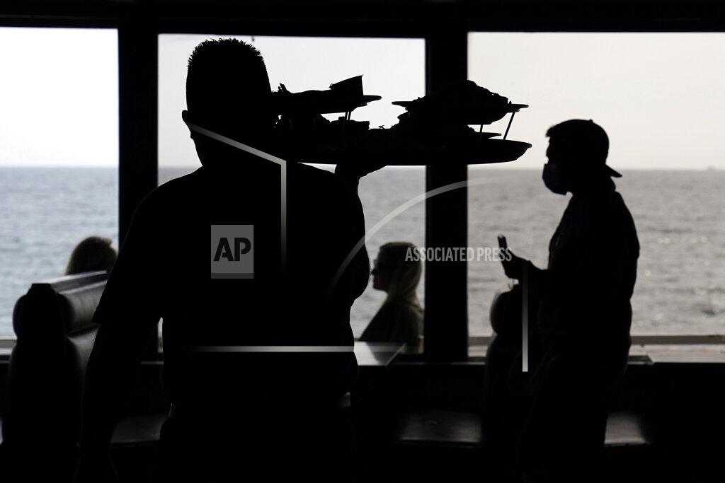 Mark J. Terrill FILE - In this March 14, 2021, file photo wait staff walk through an empty dining room as diners eat outside in front of beach views at Gladstones restaurant in the Pacific Palisades section of Los Angeles. Los Angeles County can reopen even more businesses while expanding how many people are allowed to dine indoors or catch a movie, California public health officials announced Tuesday, March 30, 2021. The county of 10 million people was one of several that moved into the state's orange tier, which is the second-least restrictive of California's four-tier system. (AP Photo/Mark J. Terrill)
