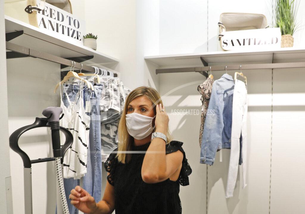 FILE - In this Wednesday, May 13, 2020, photo, Amy Witt, owner of the Velvet Window, takes a break from steam-sanitizing clothes to tend to a customer, in Dallas. For small retailers across the country, the coronavirus outbreak has turned an already challenging business environment into never-ending uncertainty. “It’s a rollercoaster we ride every day,” says Witt (AP Photo/LM Otero, FILE)