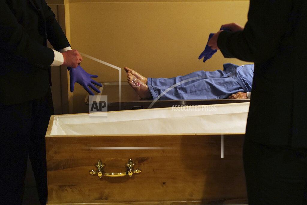 FILE - In this April 24, 2020 file photo, pallbearers, Louis Mercier, right, and Allan Pottier, left, prepare to carry the body of a 105-year-old woman as they prepare her for a funeral at a mortuary, in Paris. France is expected Thursday April 15, 2021, to pass the grim milestone of 100,000 COVID-19 deaths, after a year of hospital tensions, on-and-off lockdowns and personal loss that have left families nationwide grieving the pandemic’s unending, devastating toll. (AP Photo/Francois Mori, File)