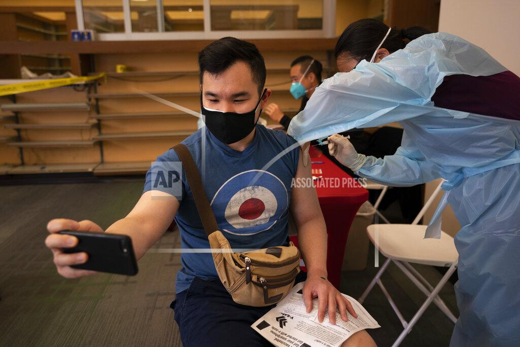 Jae C. Hong FILE - In this April 12, 2021, file photo, Freeson Wong, 31, takes a selfie as he receives a dose of the Moderna vaccine at a vaccination center in the Chinatown neighborhood of Los Angeles. The United States opened more distance between itself and much of the rest of the world on Thursday, April 15, nearing the 200 millionth vaccine administered in a months-long race to protect the population against COVID-19, even as other countries, rich and poor, struggle with stubbornly high infection rates and deaths. (AP Photo/Jae C. Hong, File)