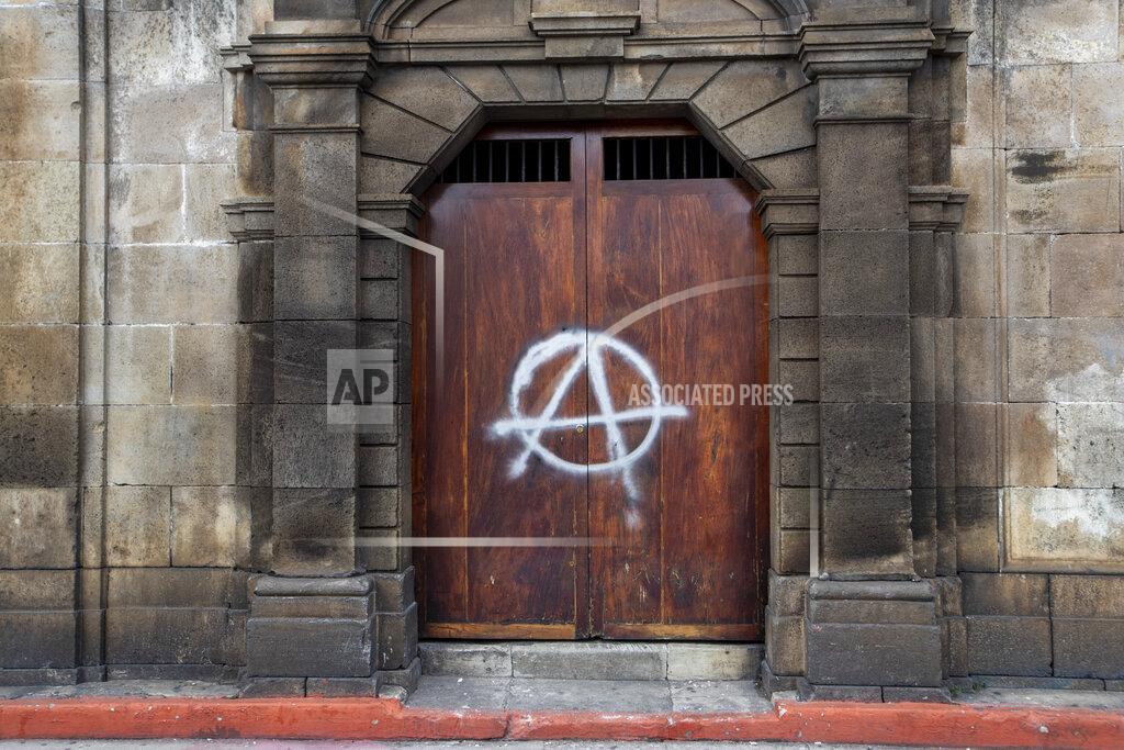 Moises Castillo A painted anarchy symbol adorns a door of the Metropolitan Cathedral in Guatemala City, Sunday, Nov. 22, 2020. Protesters also broke into the building and set Congress partially on fire amid growing demonstrations against President Alejandro Giammattei and the legislature for approving a controversial budget that cut educational and health spending. (AP Photo/Moises Castillo)