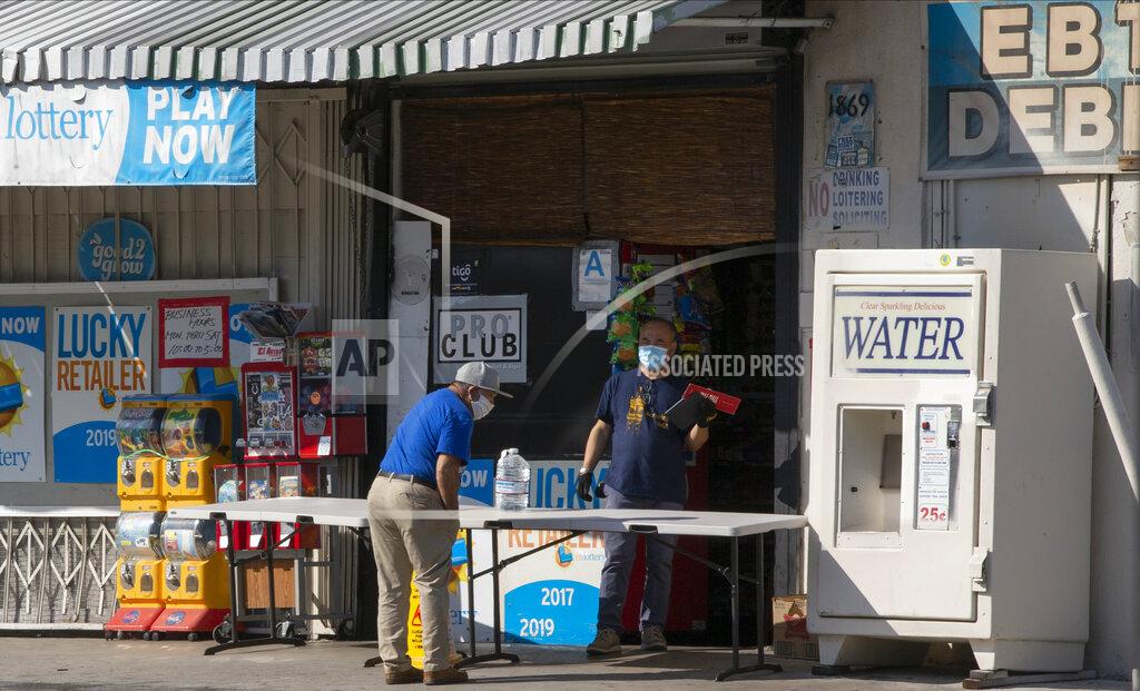 Damian Dovarganes FILE - In this April 1, 2020, file photo, a customer wears a face mask as he purchases drinking water at a "Grab-and-Go" market table in the Boyle Heights area of Los Angeles. State governments will get a big influx of federal money from the $1.9 trillion COVID-19 relief package that could suddenly enable them to undertake large, expensive projects that have long been on their to-do lists, including high-speed internet for rural areas and drinking water improvements. (AP Photo/Damian Dovarganes, File)