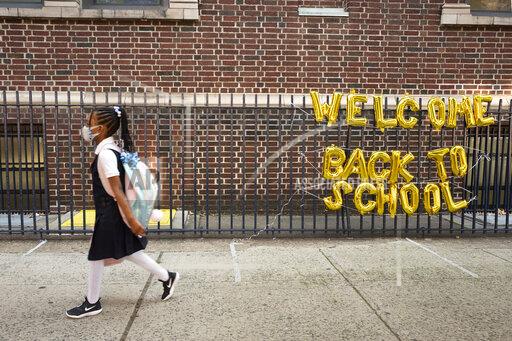 FILE - In this Sept. 13, 2021, file photo, a girl passes a "Welcome Back to School" sign as she arrives for the first day of class at Brooklyn's PS 245 elementary school in New York. COVID-19 deaths and cases in the U.S. have climbed back to where they were over the winter, fueled by children now back in their classrooms, loose mask restrictions and low vaccination levels. (AP Photo/Mark Lennihan, File)