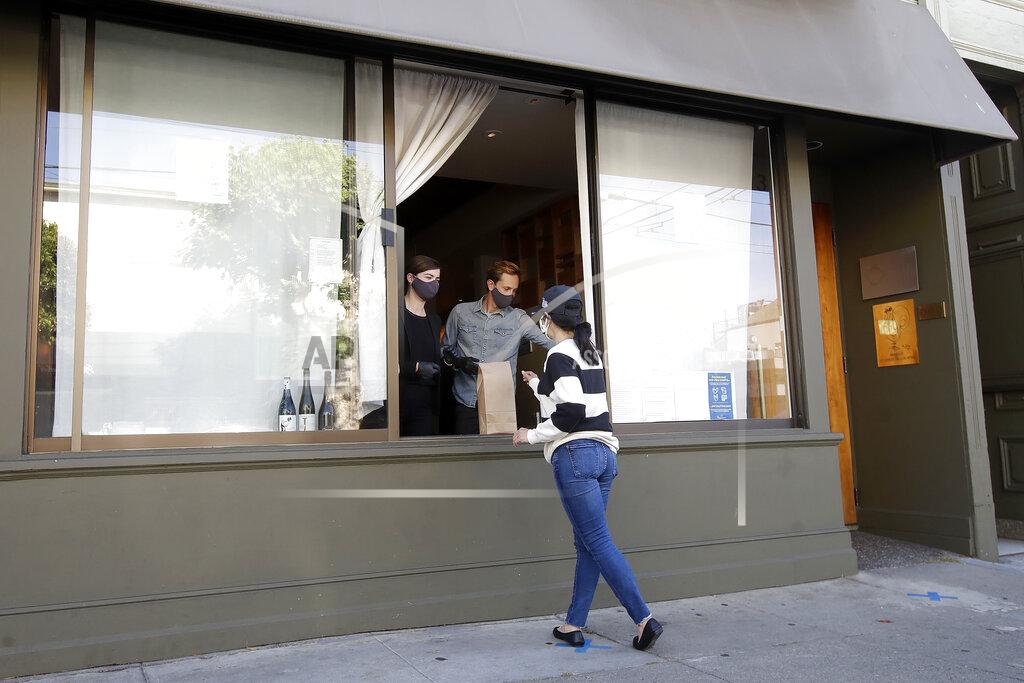 Jeff Chiu In this Thursday, June 18, 2020, photo, lead sommelier Rachel Coe, left, and service manager Antoine Mueller wear face masks as they assist a customer at the Atelier Crenn restaurant window during the coronavirus outbreak in San Francisco. Some of the world's best restaurants have had to make a quick pivot to weather the coronavirus. (AP Photo/Jeff Chiu)