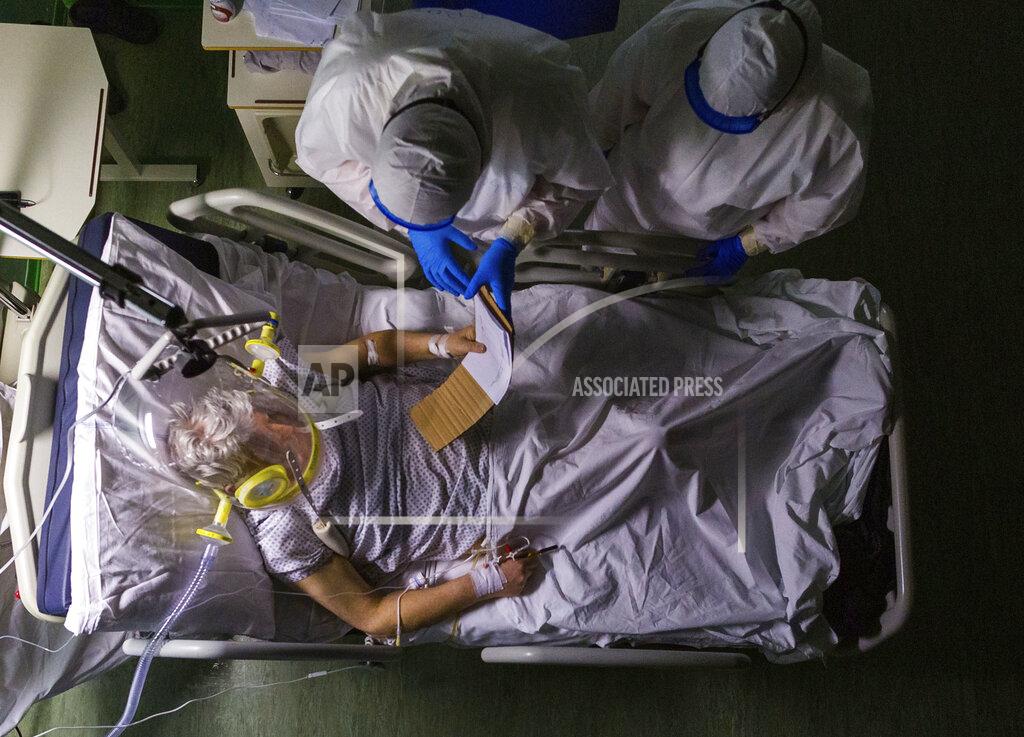 Domenico Stinellis Eighty-two-year-old patient Mario reads a note on his medical condition during a routine examination by Dr. Giovanni Passeri, upper left, and his assistant Dr. Mariaconcetta Terracina during the night shift in the COVID-19 section of the Maggiore Hospital in Parma, northern Italy, on Wednesday, April 8, 2020. Mario has been under oxygen CPAP (continuous positive air pressure) headgear ventilation and he could only communicate in writing because the hissing sound of the oxygen made it difficult for him to hear the doctor's voice. Mario's health conditions worsened since his admission on March 28. He died on the evening of April 14. (AP Photo/Domenico Stinellis)