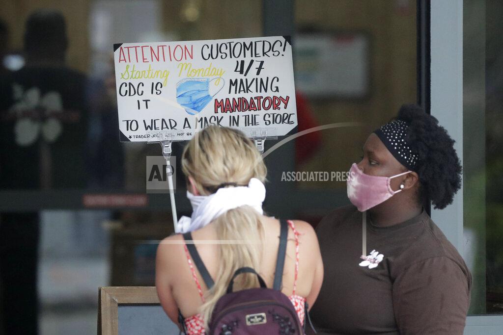 A grocery store employee, right, limits the number of customers entering the store, Tuesday, April 7, 2020, in Miami Beach, Fla. According to their website, "the City of Miami Beach has added a requirement in the latest Emergency Order, effective April 7, 2020, for all employees and customers of grocery stores, pharmacies and restaurant facilities to wear a form of covering over their nose and mouth at all times when inside these establishments." (AP Photo/Wilfredo Lee)