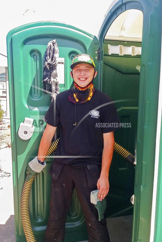 Robert Peach Donnie Settles, 27, stands near a portable toilet on July 14, 2020, which he services for his employer in Arcata, Calif. Settles lived at an emergency tent shelter for two months during COVID-19 while he saved up money for rent. Many homeless people work low-wage essential jobs on the front lines of the pandemic, putting them at higher risk of catching and possibly transmitting the virus. Many who work with these communities are reluctant to speak about this risk for fear of further stigmatizing homeless people, even though they do the front-line jobs others can avoid. (Robert Peach/Arcata House Partnership and the Howard Center For Investigative Journalism via AP)
