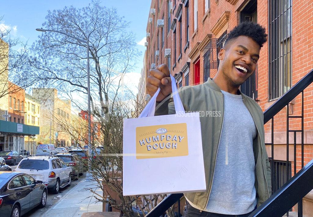 Michael Lowney Broadway performer Max Kumangai holds a bag promoting his company Humpday Dough in New York. The triple threat from the musical “Jagged Little Pill” has leaned into a fourth skill as the pandemic marches on: baking and selling his own sourdough. (Michael Lowney/Humpday Dough via AP)