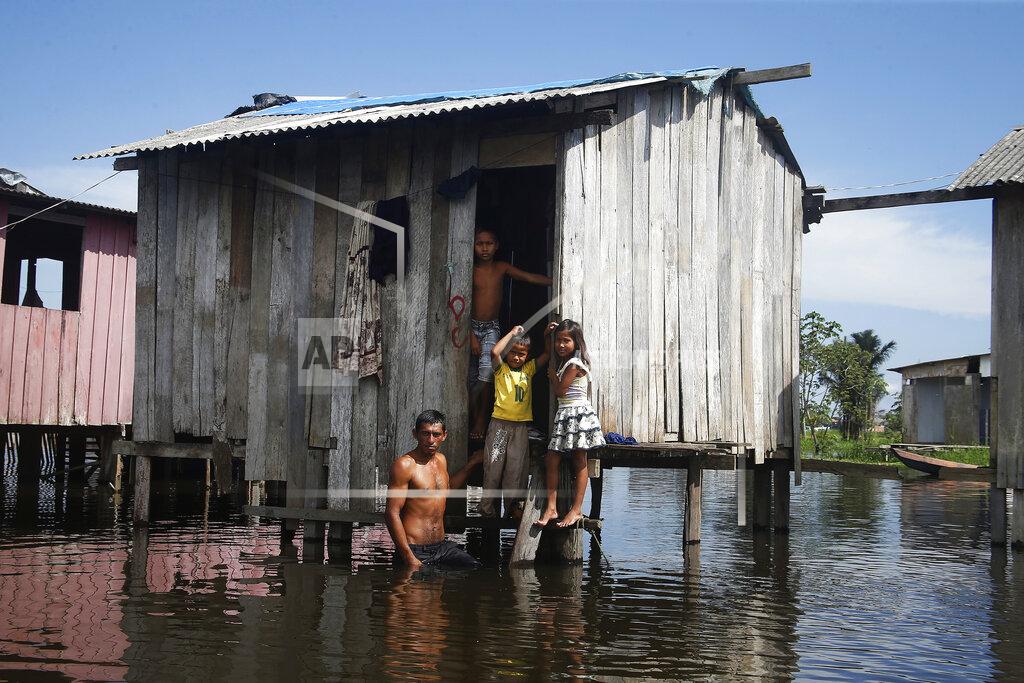 Edmar Barros Francisco Fabiano Rodrigues and his children stand on the porch of their home on a street flooded by the rise of the Negro river in Iranduba, Amazonas state, Brazil, Monday, May 23, 2022. The Amazon region is being hit hard by flooding with 35 municipalities that are facing one of their worst floods in years and the water level is expected to rise over the coming months. (AP Photo/Edmar Barros)