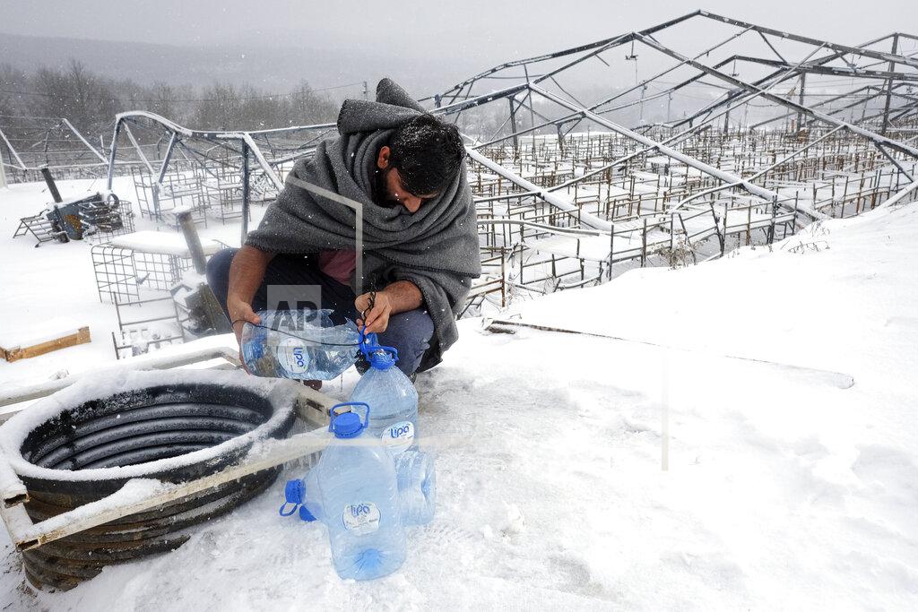 Kemal Softic A migrant uses plastic bottles to take water out of a well during a snowfall at the Lipa camp, outside Bihac, Bosnia, Monday, Jan. 11, 2021. Aid workers say migrants staying at a camp in northwestern Bosnia have complained or respiratory and skin diseases after spending days in make-shift tents and containers amid freezing weather and snow blizzards. Most of the hundreds of migrants at the Lipa facility near Bosnia's border with Croatia on Monday have been accommodated in heated military tents following days of uncertainty after a fire gutted most of the camp on Dec. 23. (AP Photo/Kemal Softic)