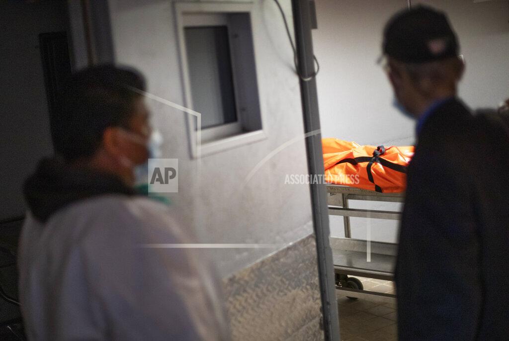 David Goldman Gravedigger Thomas Cortez, left, and Rabbi Shmuel Plafker look into the mortuary cooler after someone presumed to have died from coronanvirus arrived from a hospital as they keep pace with a surge in burials at Mount Richmond Cemetery in the Staten Island borough of New York, Tuesday, April 7, 2020. Companies that transport the dead to their final resting places are backed up, part of a chain reaction of hold-ups that includes overbooked funeral homes and cemeteries that are turning families away. (AP Photo/David Goldman)
