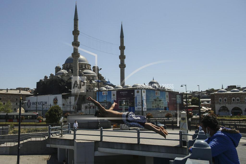Emrah Gurel Backdropped by the historical Yeni Cami (New Mosque), a youth jumps from the Galata Bridge into the Golden Horn leading to the Bosphorus Strait separating Europe and Asia, in Istanbul, Friday, May 14, 2021.Turkey is in the final days of a full coronavirus lockdown and the government has ordered people to stay home and businesses to close amid a huge surge in new daily infections. But millions of workers are exempt and so are foreign tourists. Turkey is courting international tourists during an economic downturn and needs the foreign currencies that tourism brings to help the economy as the Turkish lira continues to sink. (AP Photo/Emrah Gurel)
