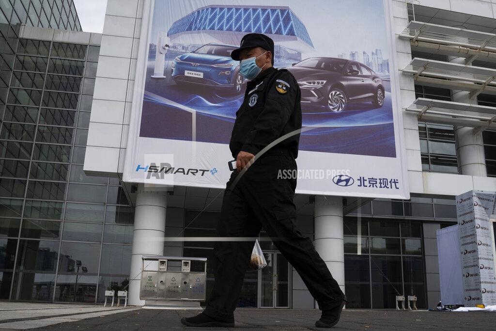 Ng Han Guan A security guard wearing a mask walks past an advertisement for the Auto China 2020 show to be held in Beijing on Thursday, Sept. 24, 2020. Auto executives are flying in early to wait out a coronavirus quarantine ahead of the Beijing auto show, the year's biggest sales event for a global industry that is struggling with tumbling sales and layoffs. (AP Photo/Ng Han Guan)