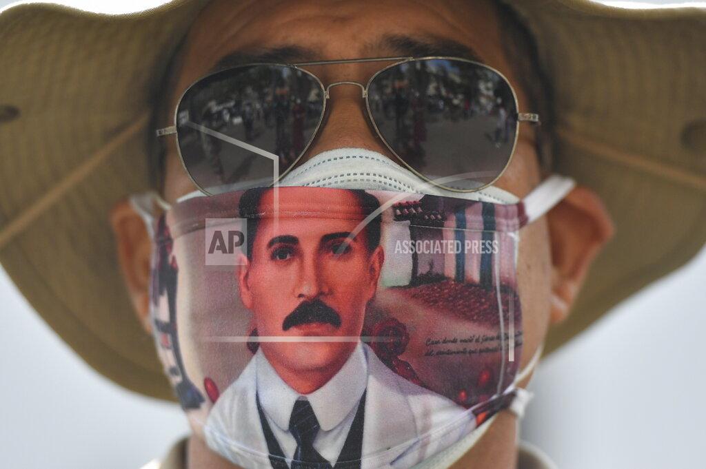 Matias Delacroix A man wears a mask featuring the image of the late, Venezuelan Dr. Jose Gregorio Hernandez, on the day of his Beatification ceremony outside the church that guards his remains in La Candelaria area of Caracas, Venezuela, Friday, April 30, 2021. Known as the "doctor of the poor, Hernandez will be beatified Friday by the Catholic church, a step towards sainthood. (AP Photo/Matias Delacroix)