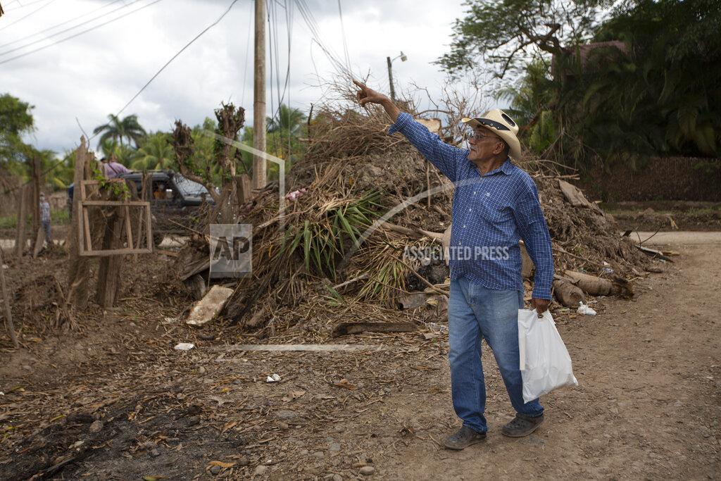 Moises Castillo Juan Antonio Ramirez, 73, points to a tree that was hit by the floods during last year's hurricanes Eta and Iota in the San Jose neighborhood of La Lima, on the outskirts of San Pedro Sula, Honduras, where banana and sugar cane workers live, Monday, Jan. 11, 2021. Ramirez's children and grandchildren were among some 30 people who spent six days stranded on a corrugated metal roof surrounded by floodwaters in November. (AP Photo/Moises Castillo)