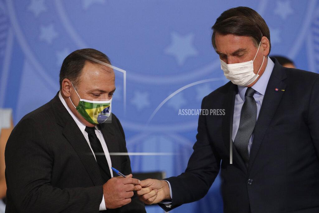 Brazil's President Jair Bolsonaro, wearing a mask to curb the spread of COVID-19, hands a pen to Health Minister Gen. Eduardo Pazuelo, left, at Planalto Presidential Palace, in Brasilia, Brazil, Wednesday, Sept. 16, 2020. After almost four months overseeing the COVID-19 response as interim health minister, Gen. Eduardo Pazuello will finally be made a full minister. (AP Photo/Eraldo Peres)