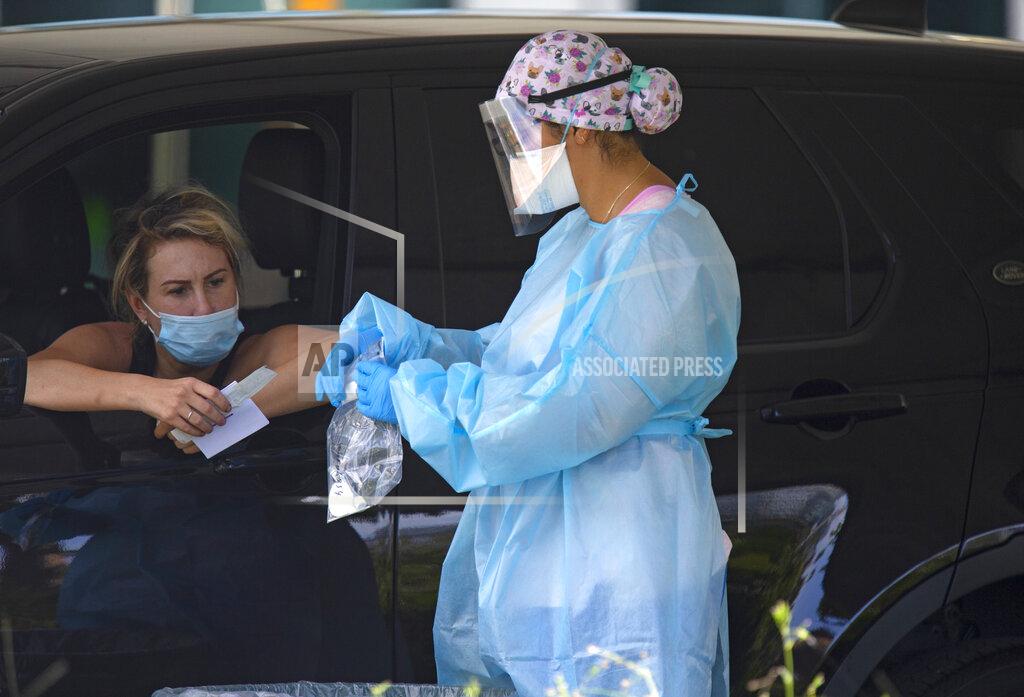 A health care worker collects a COVID-19 test sample after a person used a nasal swab for a self administered test at the COVID-19 drive-thru testing center at Miami Beach Convention Center Wednesday, Nov. 18, 2020, in Miami Beach, Fla. (David Santiago/Miami Herald via AP)