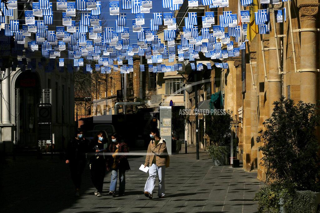 Petros Karadjias People wearing face masks walk past a church at Faneromeni square decorated with Greek flags for celebrations marking the 200th anniversary of the outbreak of the country's Independence War of Greece, in central capital Nicosia, Cyprus, Friday, March 12, 2021. Cyprus put the breaks on a wider loosening of COVID-19 restrictions by keeping middle school students at home for two more weeks as the infection rate remains high partly because of how widespread the U.K. variant has become. (AP Photo/Petros Karadjias)