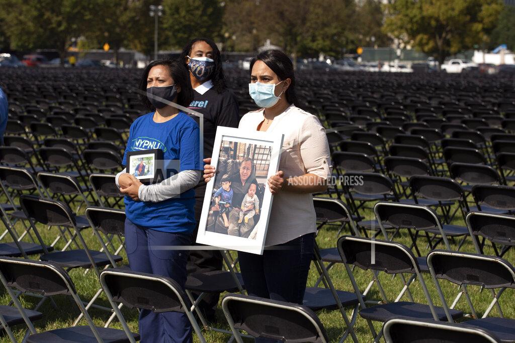 Jose Luis Magana Liza Billing, left, and Naeha Quasba hold photographs of their loved ones, who lost their life due the COVID-19, during the National COVID-19 Remembrance, at The Ellipse outside of the White House, Sunday, Oct. 4, 2020, in Washington. (AP Photo/Jose Luis Magana)