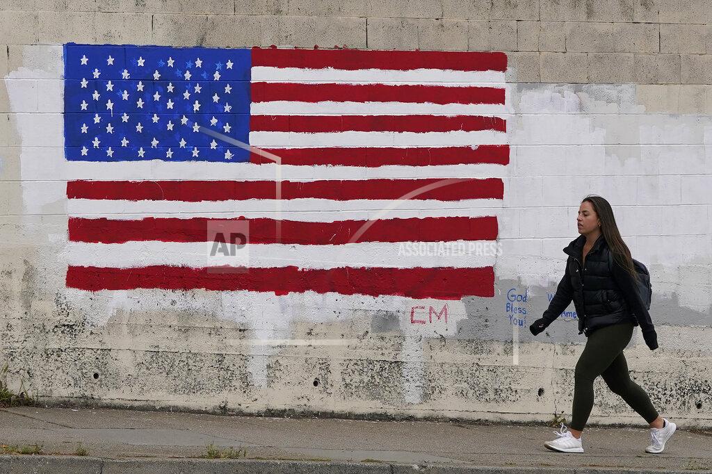 Jeff Chiu FILE - In this May 13, 2021, file photo, pedestrian walks in front of an American flag painted on a wall during the coronavirus outbreak in San Francisco. A number of states immediately embraced new guidelines from the CDC that say fully vaccinated people no longer need to wear masks indoors or out in most situations. But other states - and some businesses _ are taking a wait-and-see attitude. (AP Photo/Jeff Chiu, File)