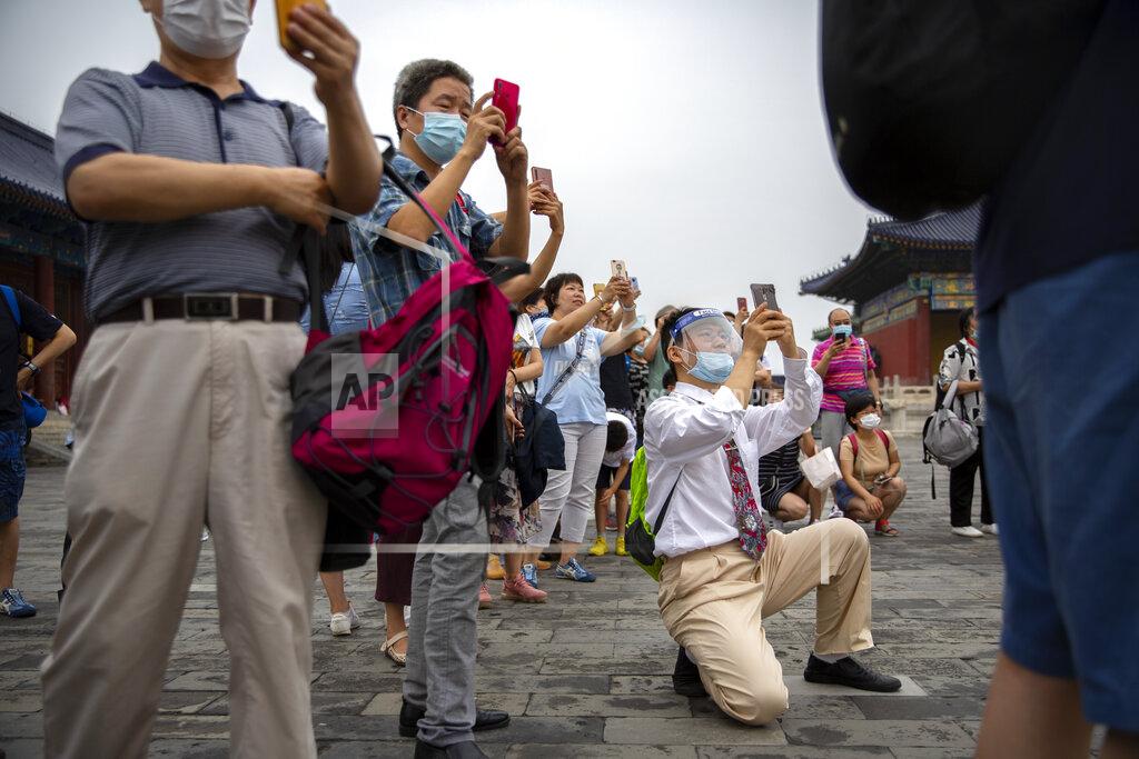 Mark Schiefelbein Parents wearing face masks to protect against the coronavirus take photos of students as they pose for a group photo at the Temple of Heaven in Beijing, Saturday, July 18, 2020. Authorities in a city in far western China have reduced subways, buses and taxis and closed off some residential communities amid a new coronavirus outbreak, according to Chinese media reports. They also placed restrictions on people leaving the city, including a suspension of subway service to the airport. (AP Photo/Mark Schiefelbein)