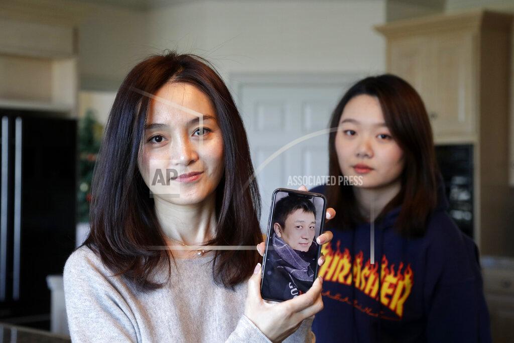 Elaine Thompson Jodie Chen, left, holds a photo of her husband, Daniel Hsu, as their daughter, Mandy Luo, looks on in their home in Issaquah, Wash., on Monday, April 13, 2020. The family is waiting for husband and father Daniel Hsu to be allowed to leave China and return home. (AP Photo/Elaine Thompson)