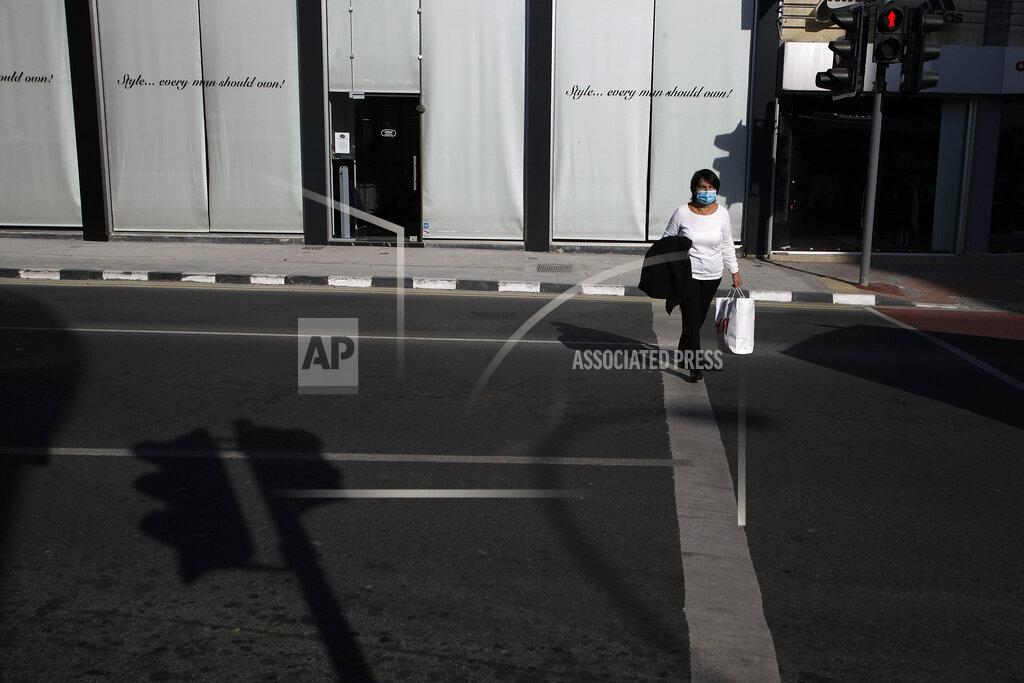 Petros Karadjias A woman wearing face mask crosses a street in central Nicosia, Friday, Jan. 8, 2021. Cyprus is returning to lockdown mode for the remainder of the month with daytime restrictions on movement and a shuttering of schools after the country's health minister conceded that a raft of tough measures already in place including a night-time curfew weren't enough to curtail the spread of the coronavirus. (AP Photo/Petros Karadjias)