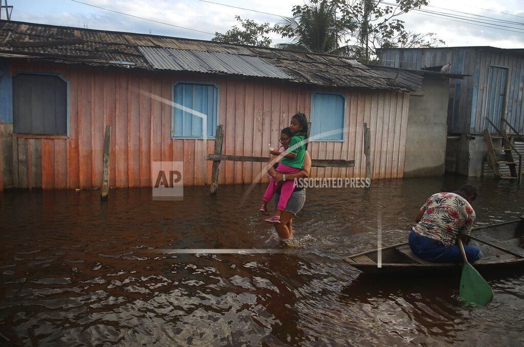 Edmar Barros A mother carries her daughter to school on a street flooded by the rise of the Negro river in Iranduba, Amazonas state, Brazil, Monday, May 23, 2022. The Amazon region is being hit hard by flooding with 35 municipalities that are facing one of their worst floods in years and the water level is expected to rise over the coming months. (AP Photo/Edmar Barros)