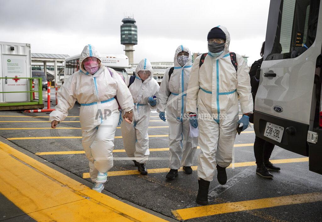 Darryl Dyck People wearing protective face masks, goggles and Tyvek suits, who said they traveled from Colombia prepare to get into a car rental company shuttle, after arriving at Vancouver International Airport in Richmond, British Columbia., Thursday, Dec. 31, 2020. Beginning January 7, air travelers arriving in Canada will be required to provide proof of a negative COVID-19 test conducted within 72 hours of boarding the plane. (Darryl Dyck/The Canadian Press via AP)