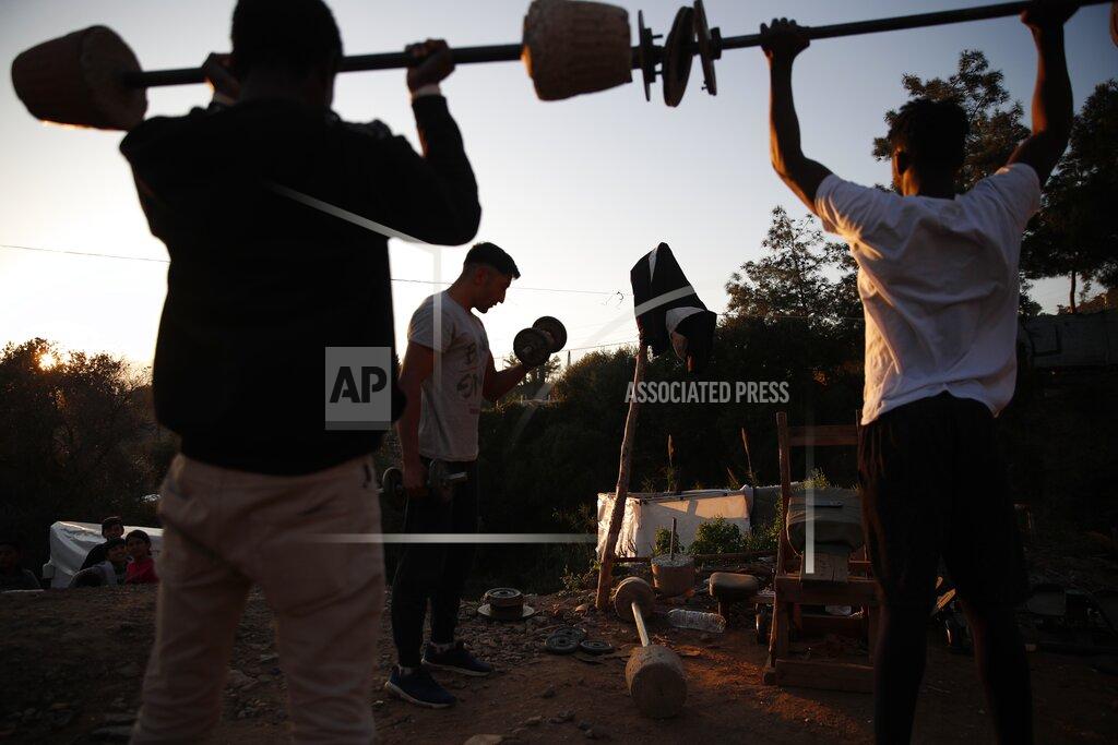 Thanassis Stavrakis Migrants lift weights at a makeshift gym outside the perimeter of the overcrowded refugee camp at the port of Vathy on the eastern Aegean island of Samos, Greece, Tuesday, Feb. 23, 2021. On a hill above a small island village, the sparkling blue of the Aegean just visible through the pine trees, lies a boy’s grave. His first ever boat ride was to be his last - the sea claimed him before his sixth birthday. His 25-year-old father, like so many before him, had hoped for a better life in Europe, far from the violence of his native Afghanistan. But his dreams were dashed on the rocks of Samos, a picturesque Greek island almost touching the Turkish coast. Still devastated from losing his only child, the father has now found himself charged with a felony count of child endangerment. (AP Photo/Thanassis Stavrakis)