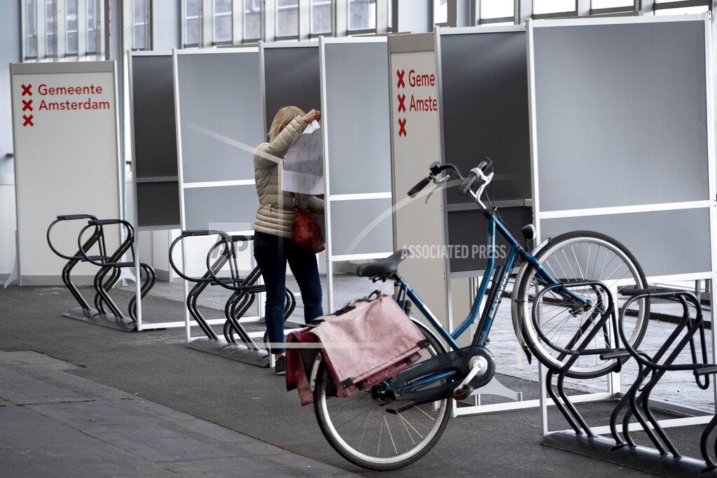 Peter Dejong A woman prepares to cast her ballot in ride through polling station for bicycles in Amsterdam, Netherlands, Monday, March 15, 2021. Polling stations opened across the Netherlands early Monday in a general election that has been spread over three days to allow people to vote safely during the coronavirus pandemic. (AP Photo/Peter Dejong)
