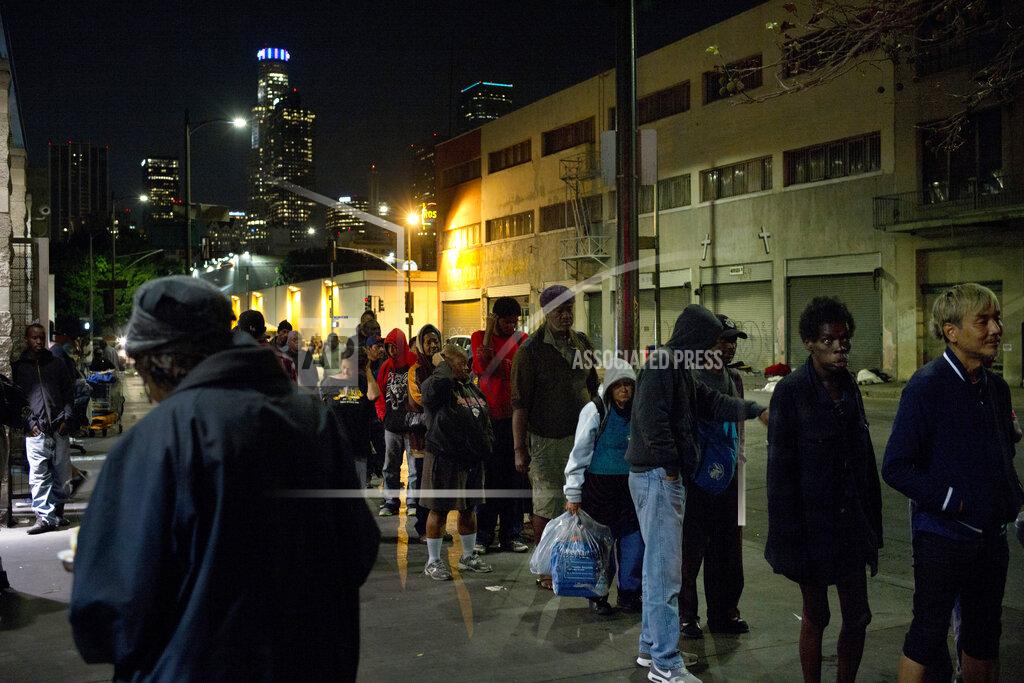 FILE - In this Sept. 19, 2017, file photo, people line up for free food being given out in an area of downtown Los Angeles known as Skid Row. A fed up federal judge says a rain storm during the last week of January 2021 created "extraordinarily harsh" conditions for homeless residents of Los Angeles and he has ordered city officials to meet with him at a Skid Row shelter to discuss how to address the worsening crisis of people living on the streets. (AP Photo/Jae C. Hong,File)