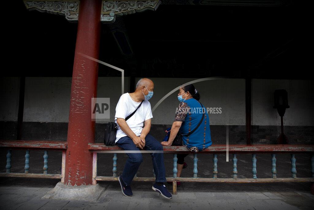 Mark Schiefelbein People wearing face masks to protect against the coronavirus sit on a railing at the Temple of Heaven in Beijing, Saturday, July 18, 2020. Authorities in a city in far western China have reduced subways, buses and taxis and closed off some residential communities amid a new coronavirus outbreak, according to Chinese media reports. They also placed restrictions on people leaving the city, including a suspension of subway service to the airport. (AP Photo/Mark Schiefelbein)